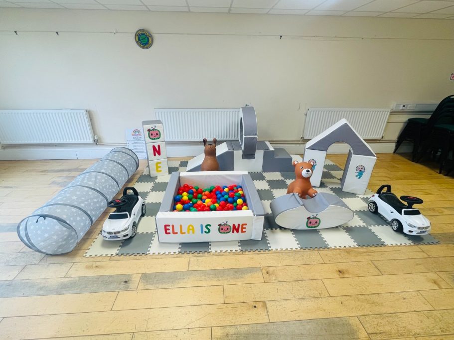 Grey and white soft play with slide, ball pit, hoppers, castle blocks, ride on cars, and a tunnel, styled for a Cocomelon party. 