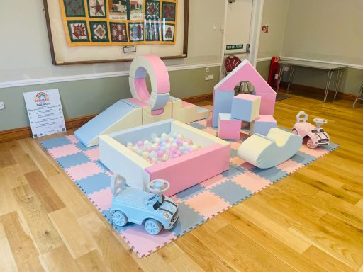 Pastel soft play setup in pink, blue, and yellow with a ball pit, slide, castle blocks, rocker and cars.