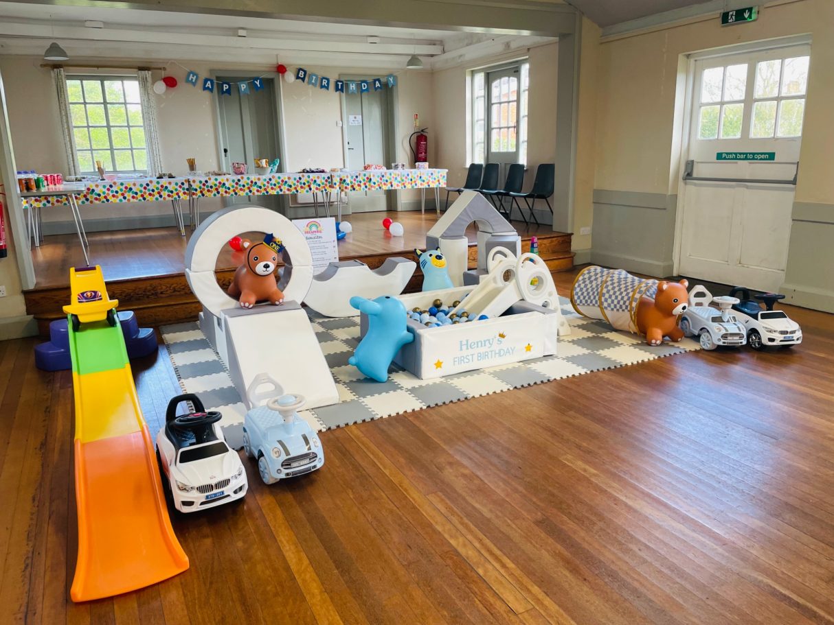 Indoor play area featuring various toys and play structures on a wooden floor.