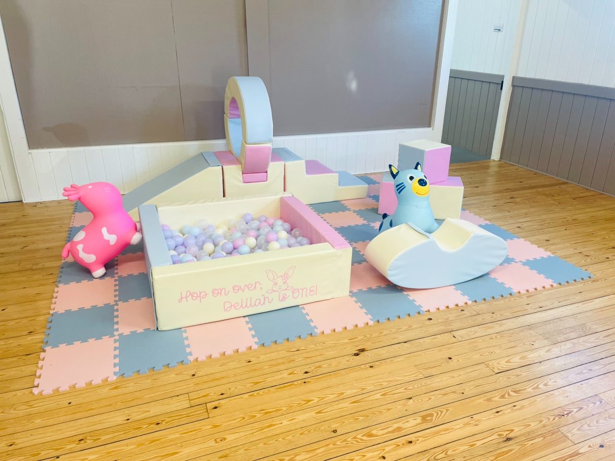 Colourful play area with soft blocks, mini structures, and plush toys on a foam mat.